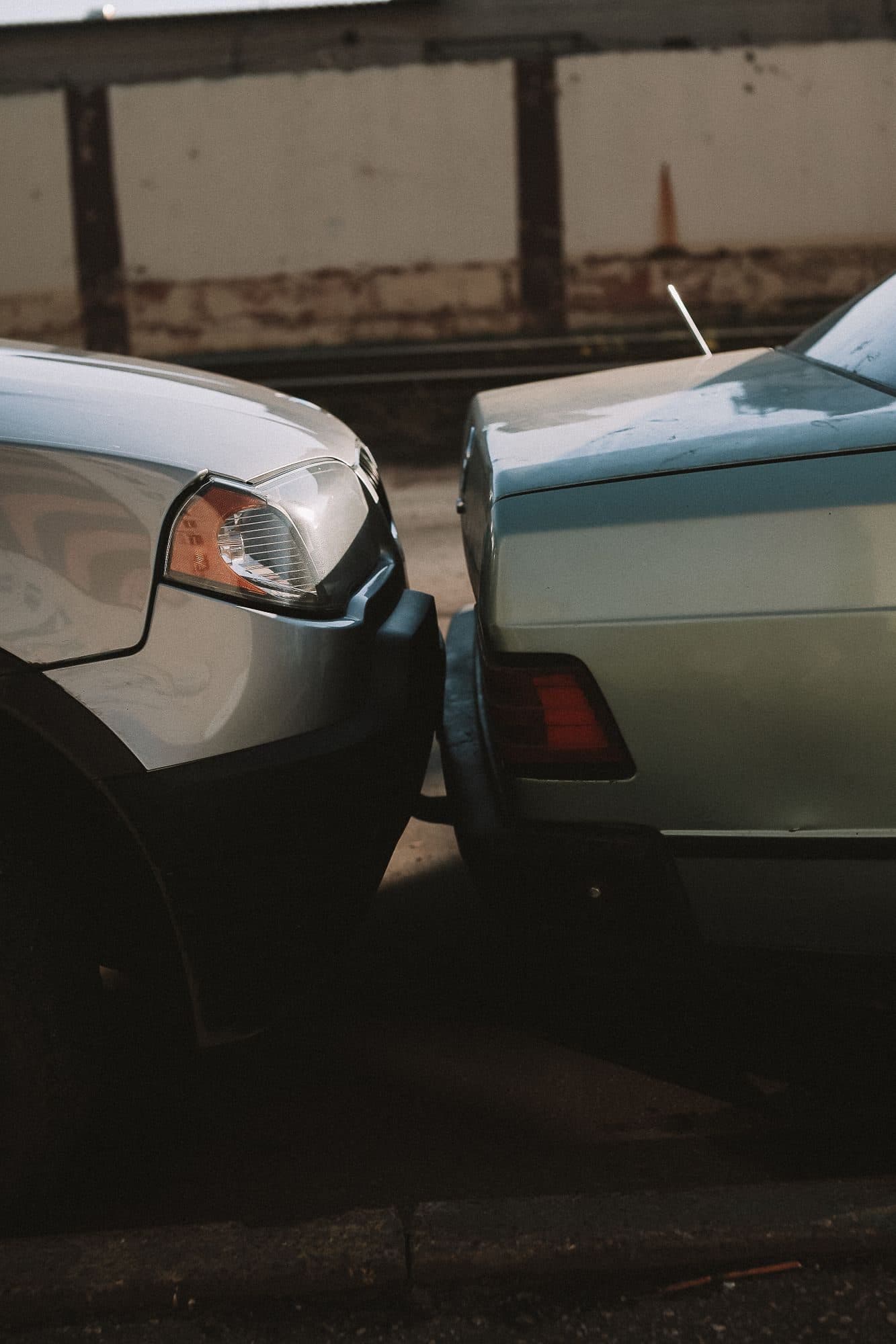 Frente de um carro encostada no para-choque traseiro de outro, em uma rua ao fim da tarde